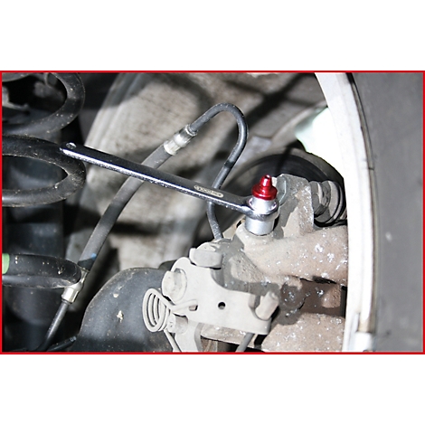 Nahaufnahme einer Person, die mit einem Schraubenschlüssel an einem Bremssattel arbeitet. Roter Nippel, metallische Teile.